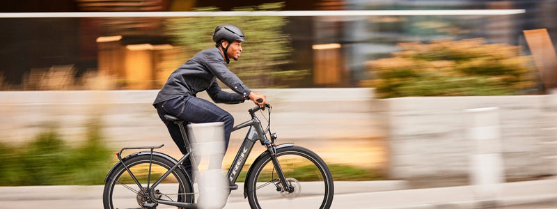 Mies kulkee sähköpyörällä pyörätiellä. Tausta on sumentunut kovasta vauhdista