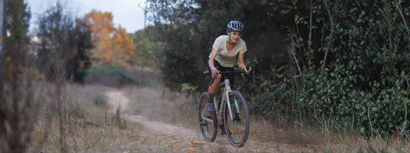 Nainen pyöräilee gravel pyörällään kapealla metsäpolulla