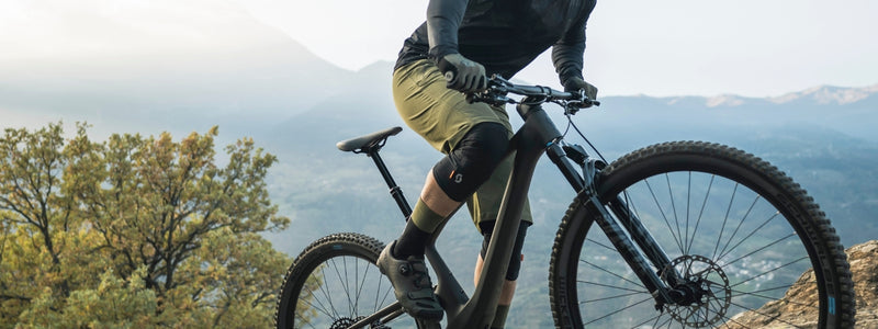 Mies pyöräilee maastopyörällä, shortsis ja polvenlämmittimet yllään