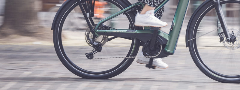 Henkilö pyöräilee kadulla, ja kuva on kohdistettu pyörän ketjusuojaan