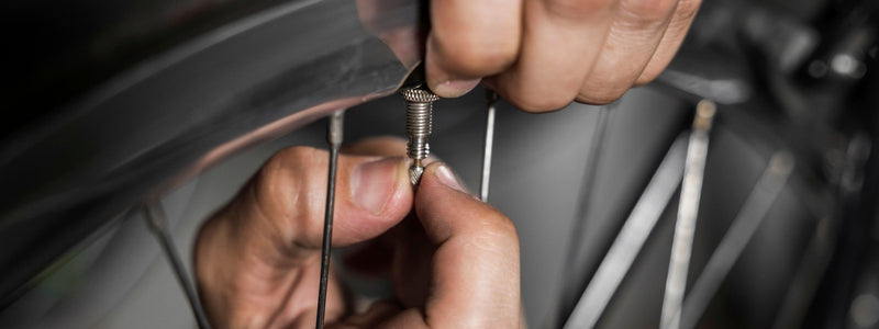 Mies avaa pyörän venttiiliä. Tilanne kuvattu läheltä